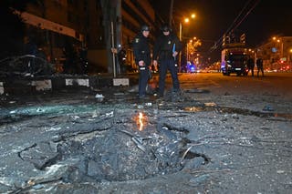 Police officers stand after the explosion near a crater